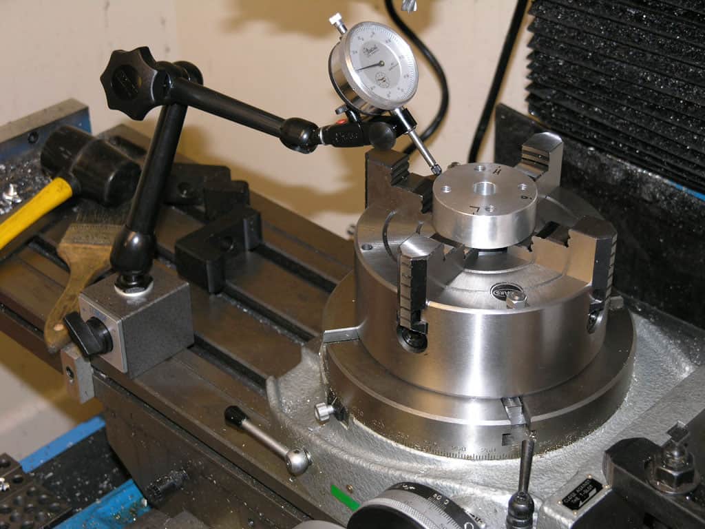 Precision measuring device with central hole and rotating dial, accompanied by a black clamp and yellow tool.