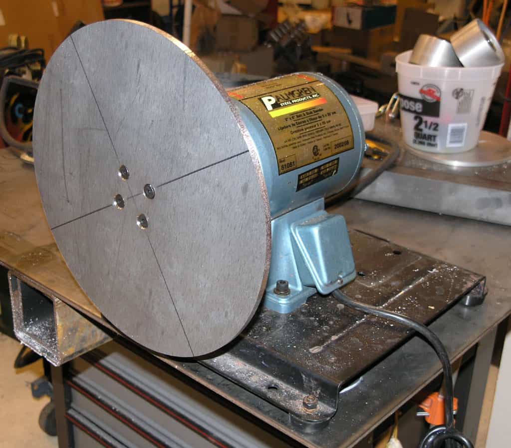 A blue and gold 2" bore buffing machine with a silver wheel on a metal table in a workshop.