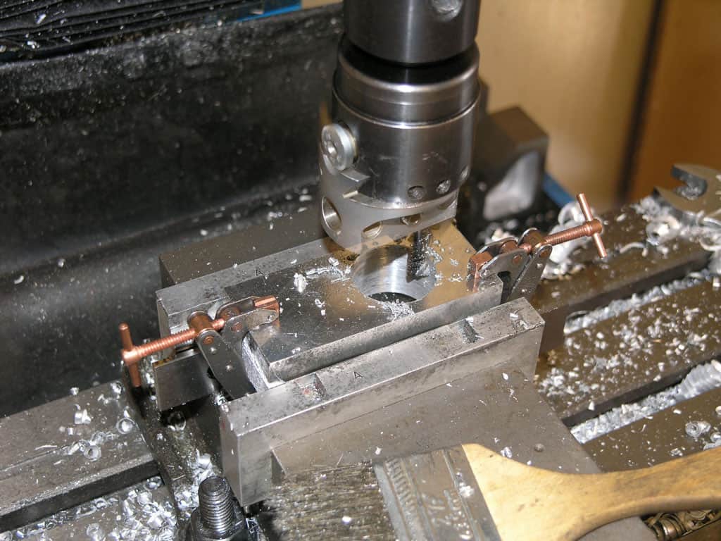 Metalworking setup with drill press or milling machine and workpiece secured in vice with copper clamps.