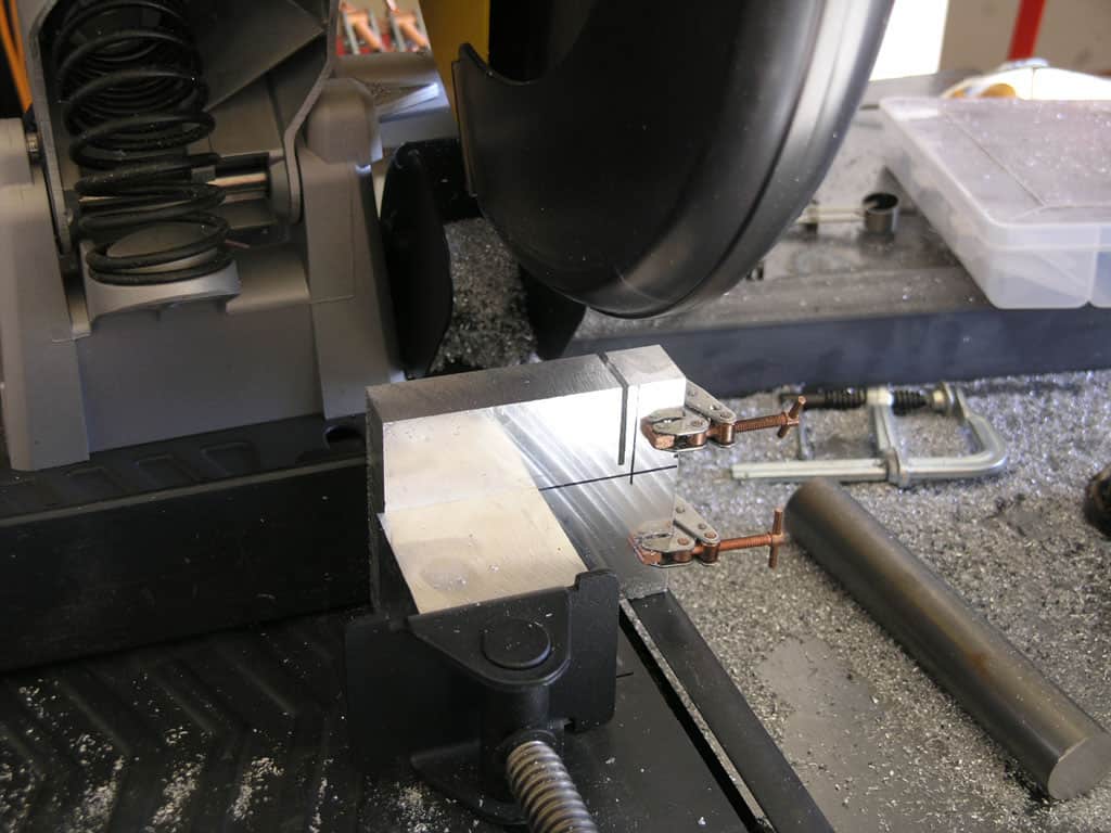 Black metal vise with silver object held in a workshop with tools and machinery.