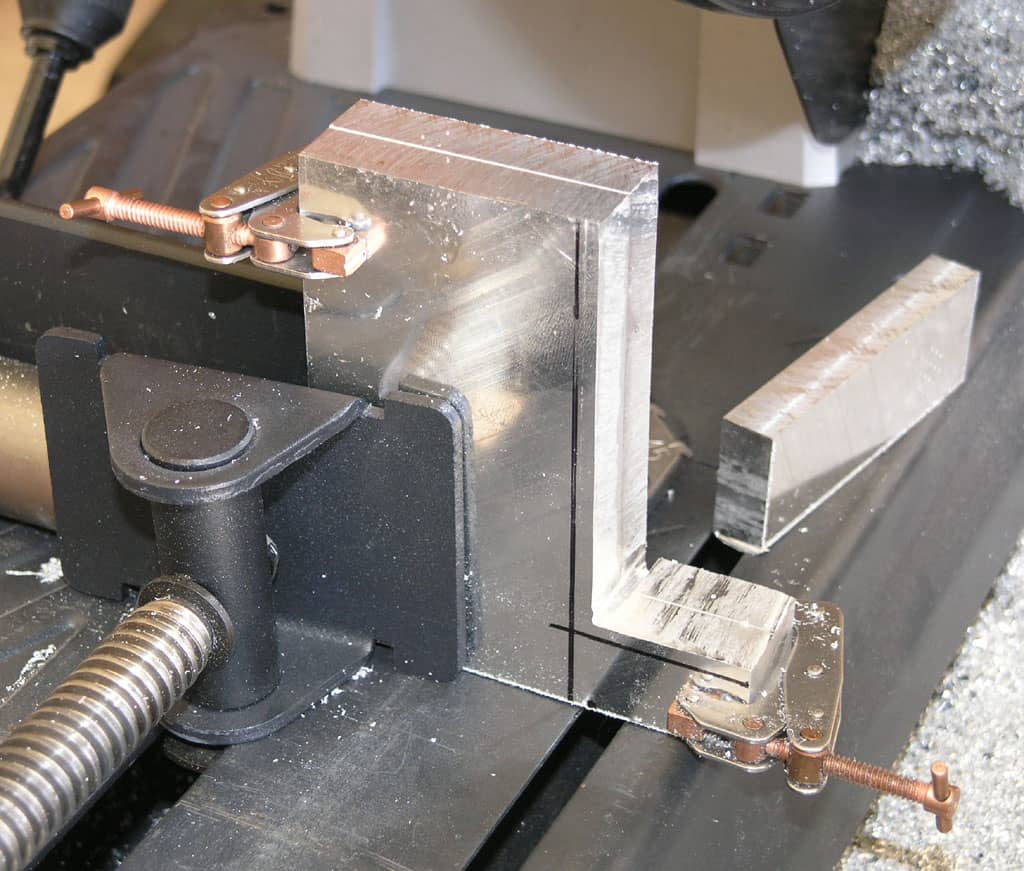 Metalworking vise holding rectangular aluminum metal with copper-clamped jaws.