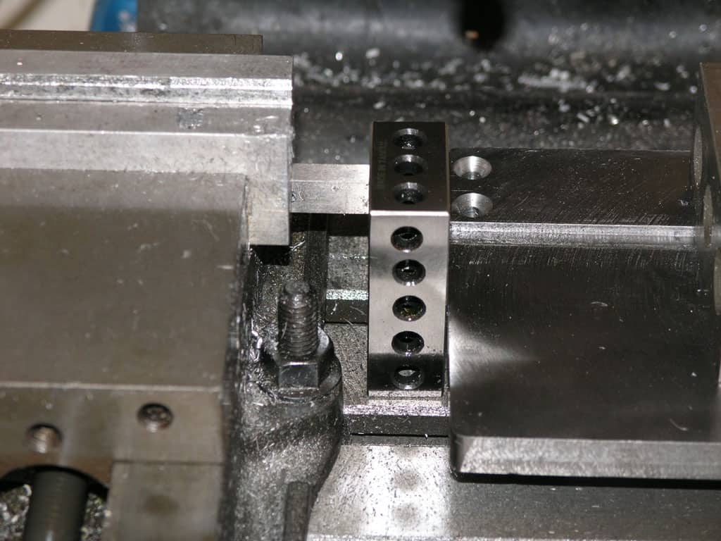 Metal component with holes on a machinery surface, made of shiny silver metal.