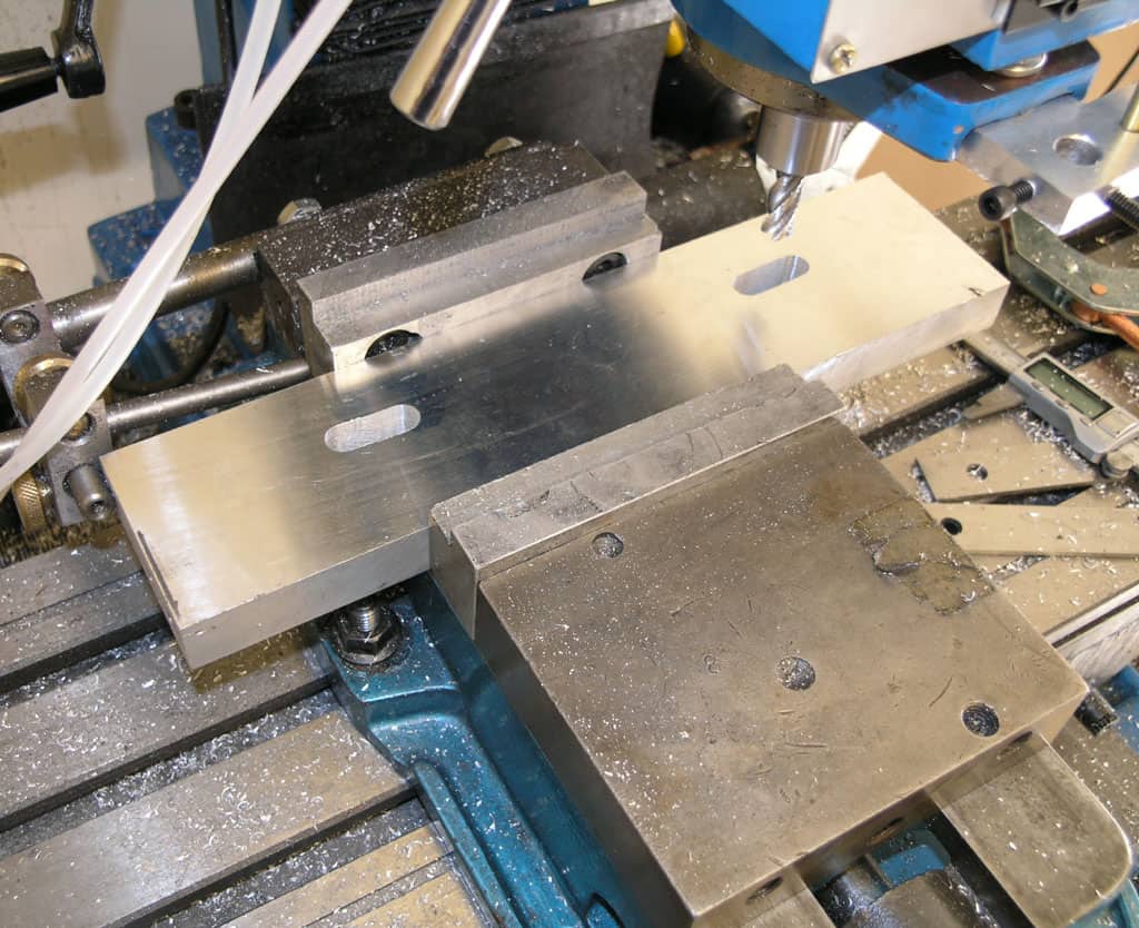 Milling machine table with blue vise and silver metal pieces.