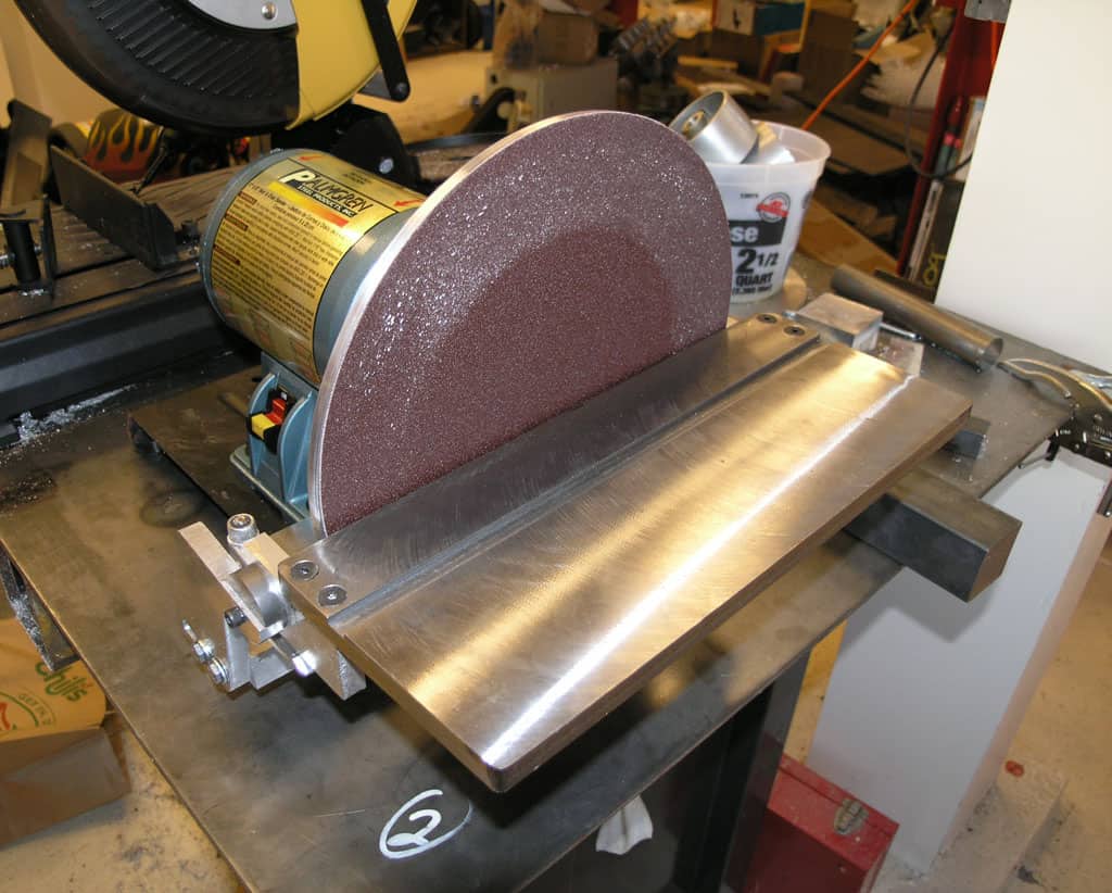 A belt sander with a metal base and long, flat table in a workshop setting.