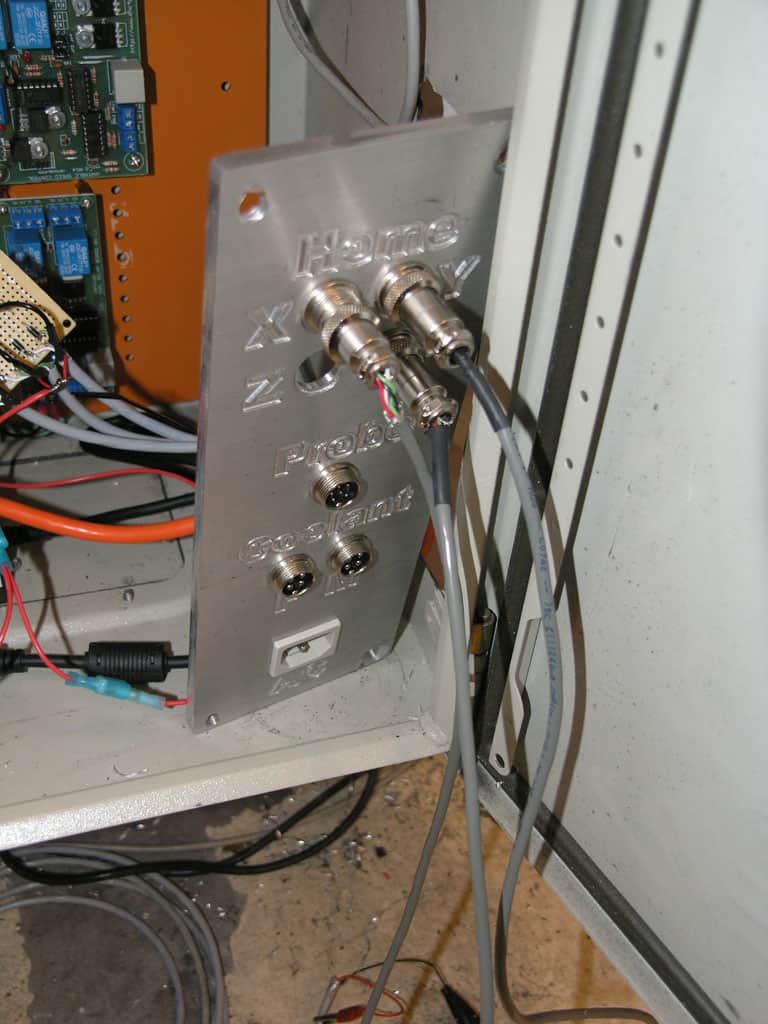 Metal plate with circular openings and attached connectors and wires in a machine setup.