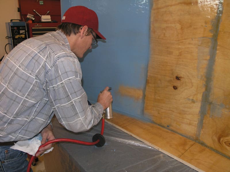A man applies paint with an airbrush in a workshop with machinery and tools.