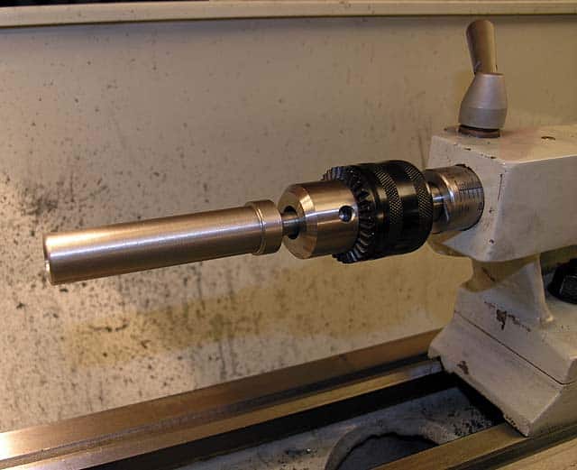 Metal part being machined on a lathe with smooth cylindrical shape.