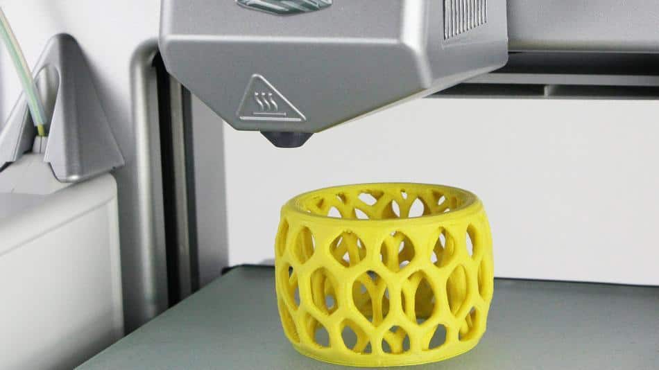 A 3D printer creates a yellow object with holes.