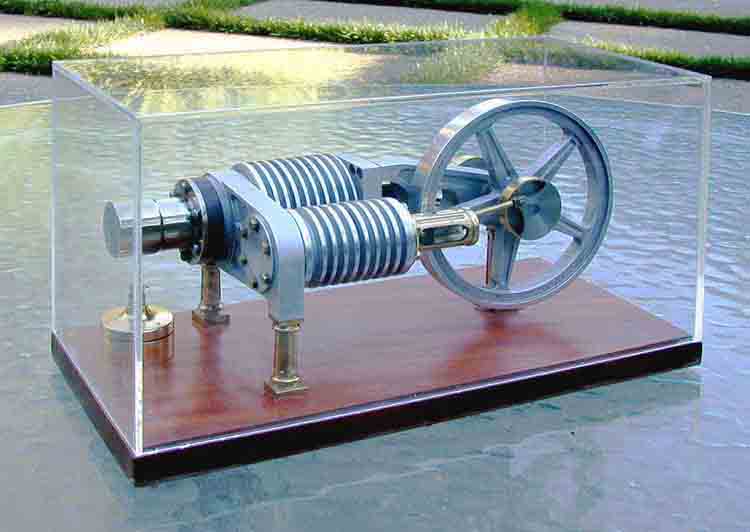 Antique drill press in glass display case with wooden base and metal components, large wheel on right side, smaller wheel on left.