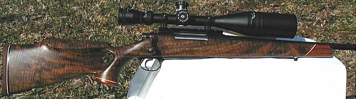 A rifle with a wooden stock and scope on a grassy surface.