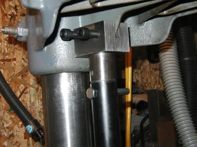 Metal component with black knob and silver cylinder on OSB board.