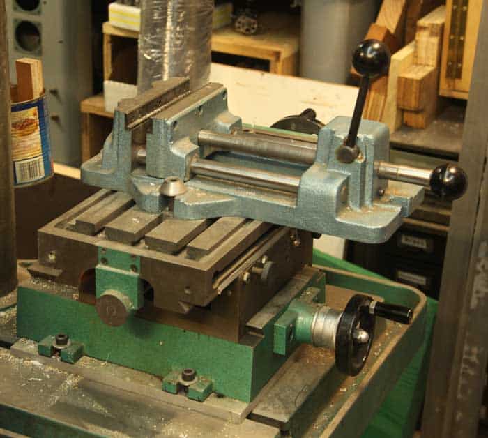Green and gray metalworking vise with vice jaw attached to a metal machine.