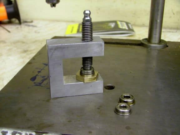 Metal clamp with threaded rod and nut on workbench.