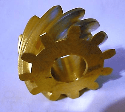 Golden-colored gear on light purple background with 12 rounded teeth and notched tips, featuring minor surface imperfections.