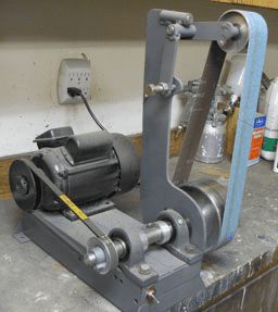 Gray metal belt sander with angled rollers on workbench.