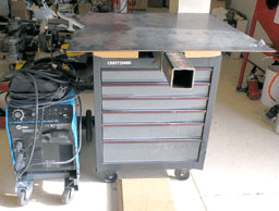 Metal toolbox on wheels with drawers and power tool in machine shop or garage.