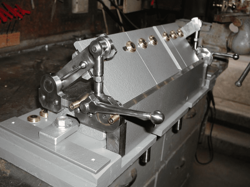 Industrial machine with lever and small holes on metallic surface in workshop setting.