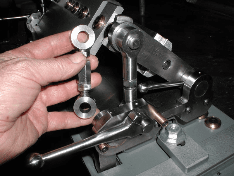 A hand holding a small metal component with holes.