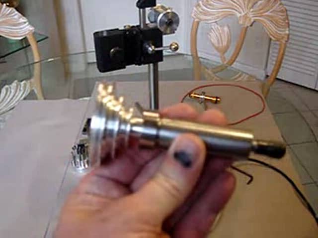 A person's hand holds a metal object with a round end featuring a small hole in the center, against a white background.