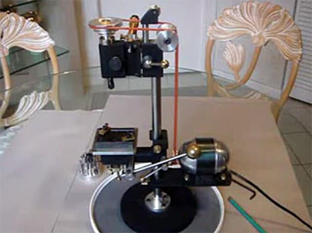 A vintage record player with a metal tonearm and headshell, surrounded by mechanical parts on a table.