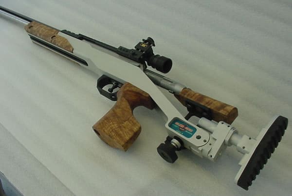 Precision rifle with wooden stock and metal barrel on a white surface, featuring a mounted high-powered scope.