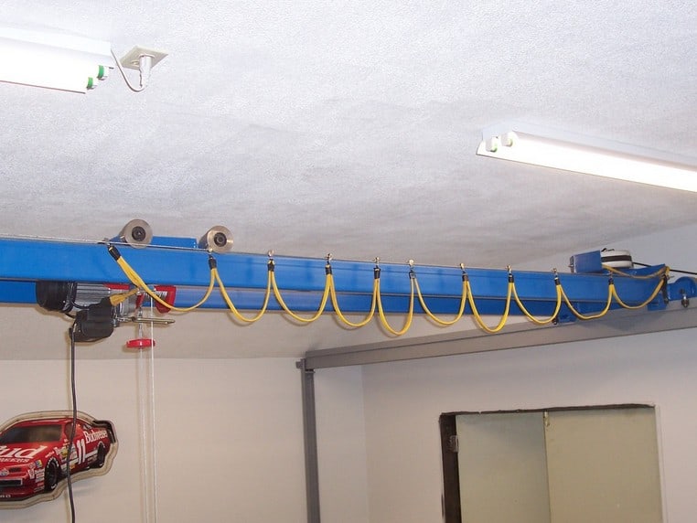 Blue garage door opener track with yellow cords and a red handle, mounted in a well-lit workshop or storage area.