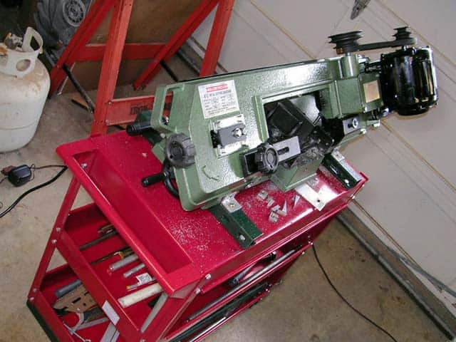 A bandsaw mounted on a red table in an industrial setting with green machine, black blade guide, and silver metal components.