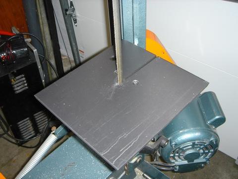 Gray metal table with small circular opening attached to a bandsaw.