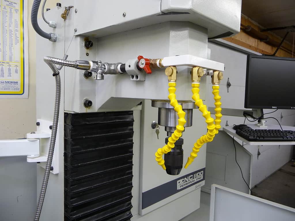 Industrial machine in workshop with yellow hoses and silver tube, black "CNC 1100" label on white body.