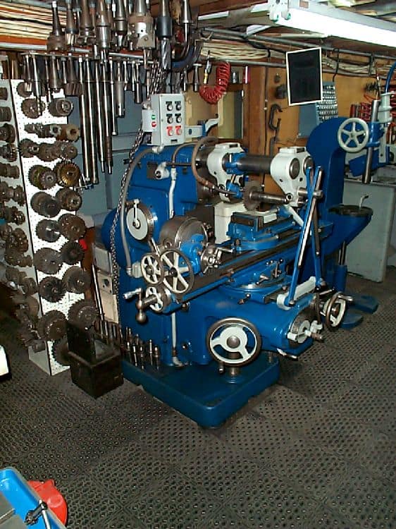 An old-style blue lathe in a workshop setting surrounded by various tools and equipment.
