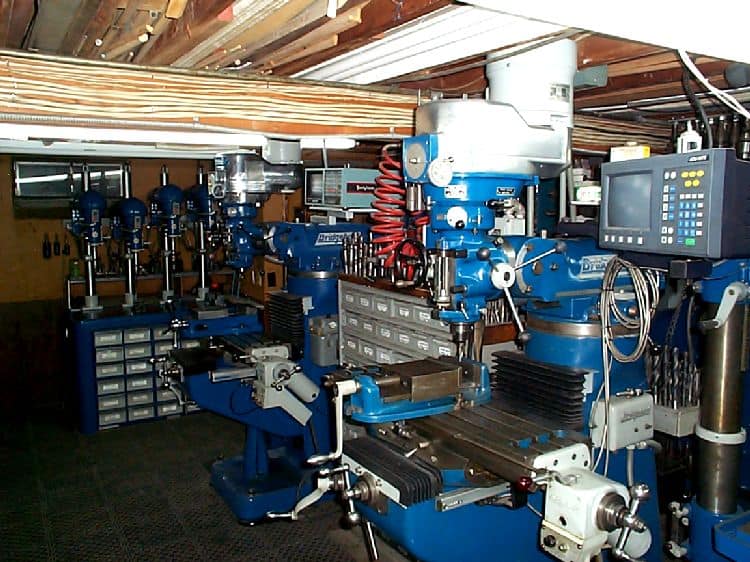 Well-equipped workshop with blue metalworking equipment, drill presses, milling machines, lathes, and other specialized tools.