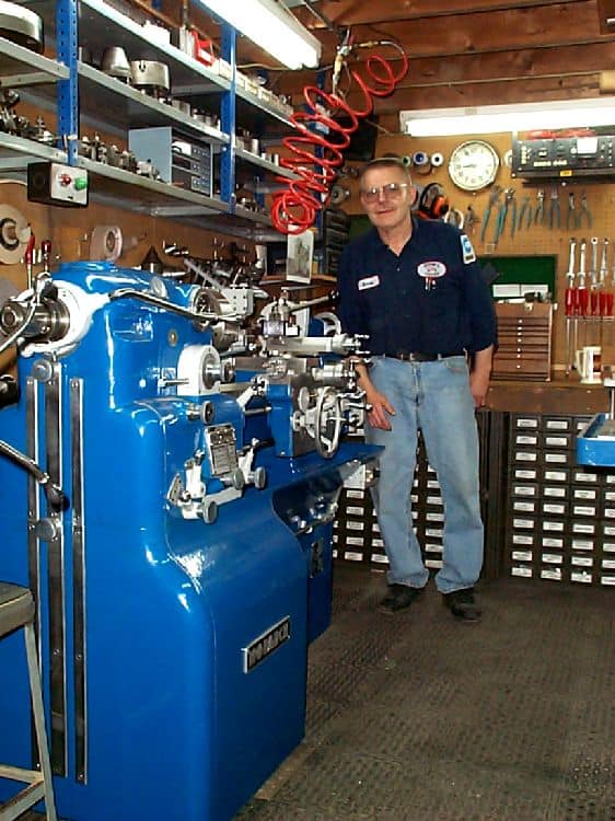 A man standing in a well-equipped workshop with lathes and metalworking tools.