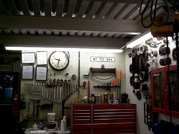 A well-organized workshop with tools and equipment on walls, dimly lit with a red toolbox and overhead storage.
