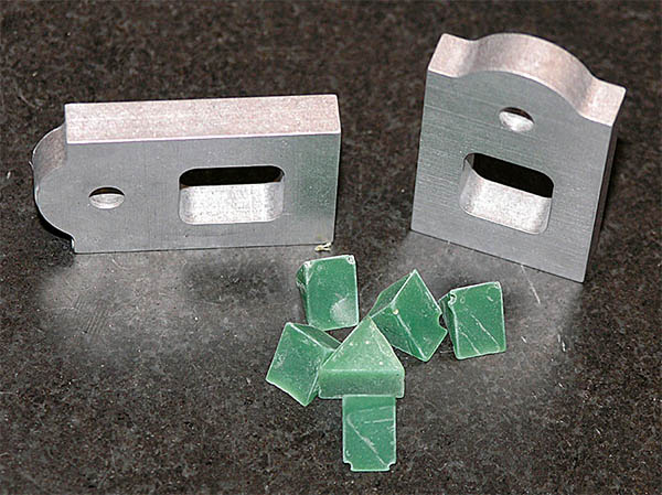 Aluminum parts with cutouts next to small green plastic resin parts for deburring metal.