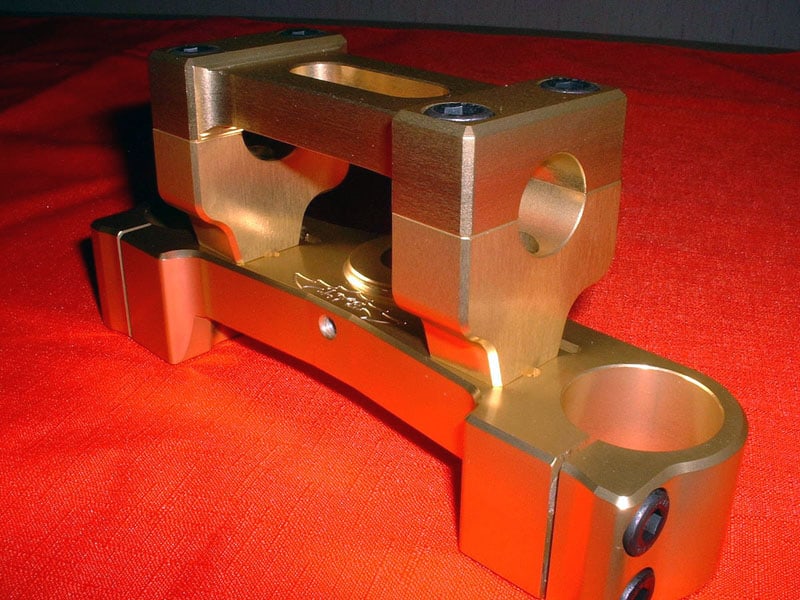 Brass or bronze clamp with two large circular holes and a small central hole, designed for Polini 50cc motorcycle engine.