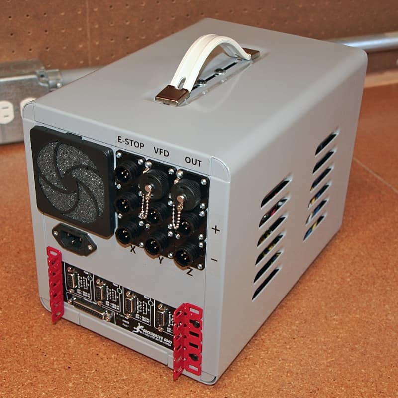 Gray box with E-STOP button, VFD connectors, and power cord on a brown surface.