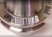 Close-up of a shiny silver metal part with a barcode-like label featuring vertical lines in varying widths.