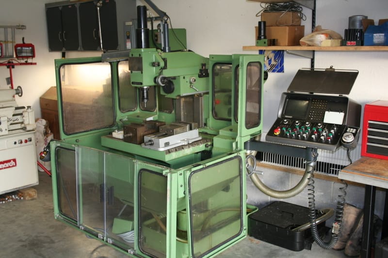 Large green milling machine in a workshop with tools and equipment.