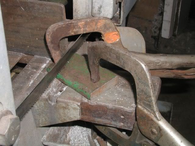 Rusty metal object with green square on top held by large metal clamp.