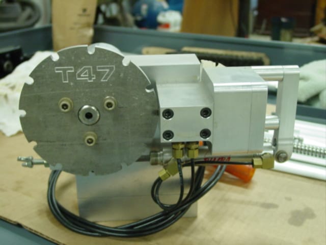 Metal device with round top and black cord, engraved "T47", displayed on workbench with assorted tools.