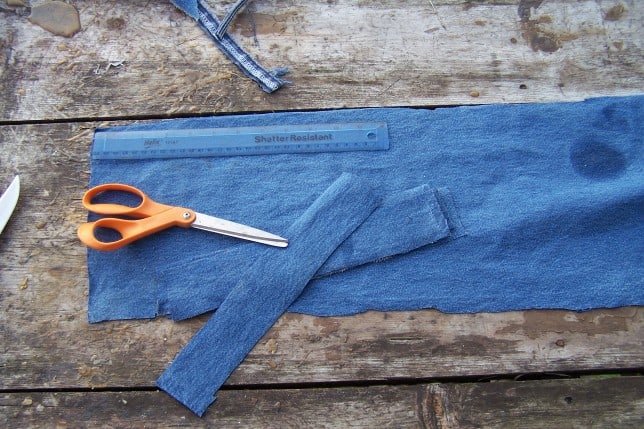 Wooden table with denim fabric, scissors, and ruler on it.