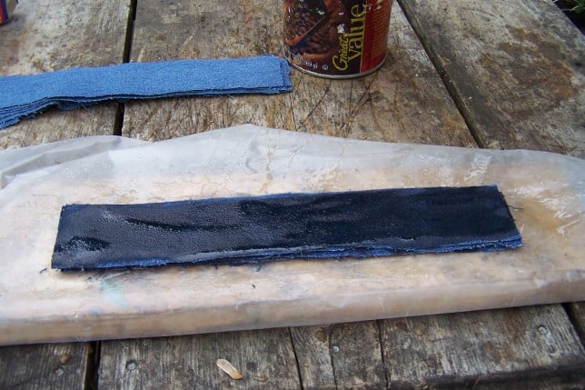 Rustic wooden table with denim fabric, glue can, and black material.