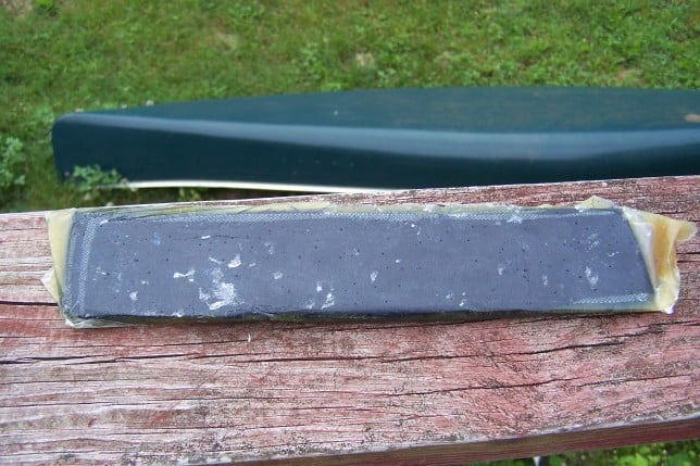 Worn metal object on weathered wooden surface with green grass backdrop.