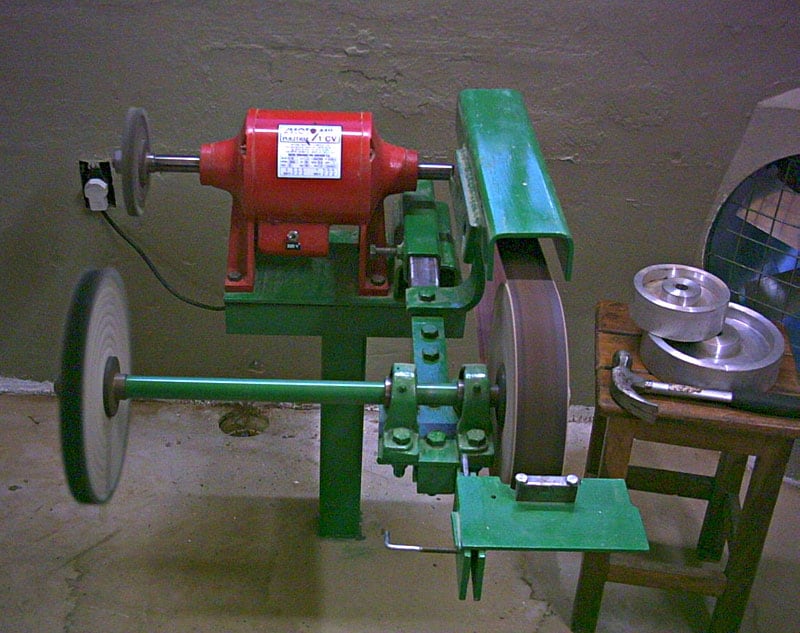 Red and green metalworking machine with two wheels on a concrete floor.