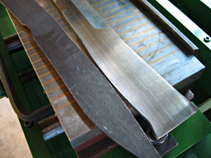 Three metal strips with rough edges arranged on a knife surface grinder machine.