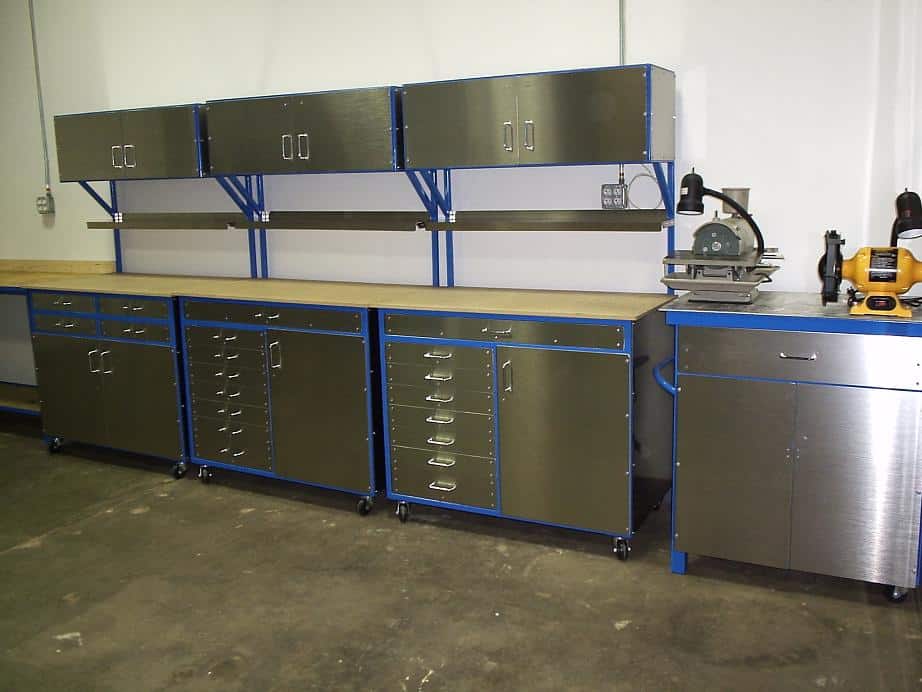 Industrial workbench with stainless steel top and blue accents, featuring a drilling station and metal fabrication equipment.