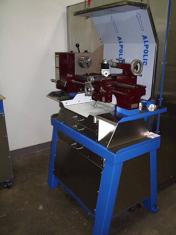 Large metalworking lathe on blue stand with four red and silver components and two black handles.