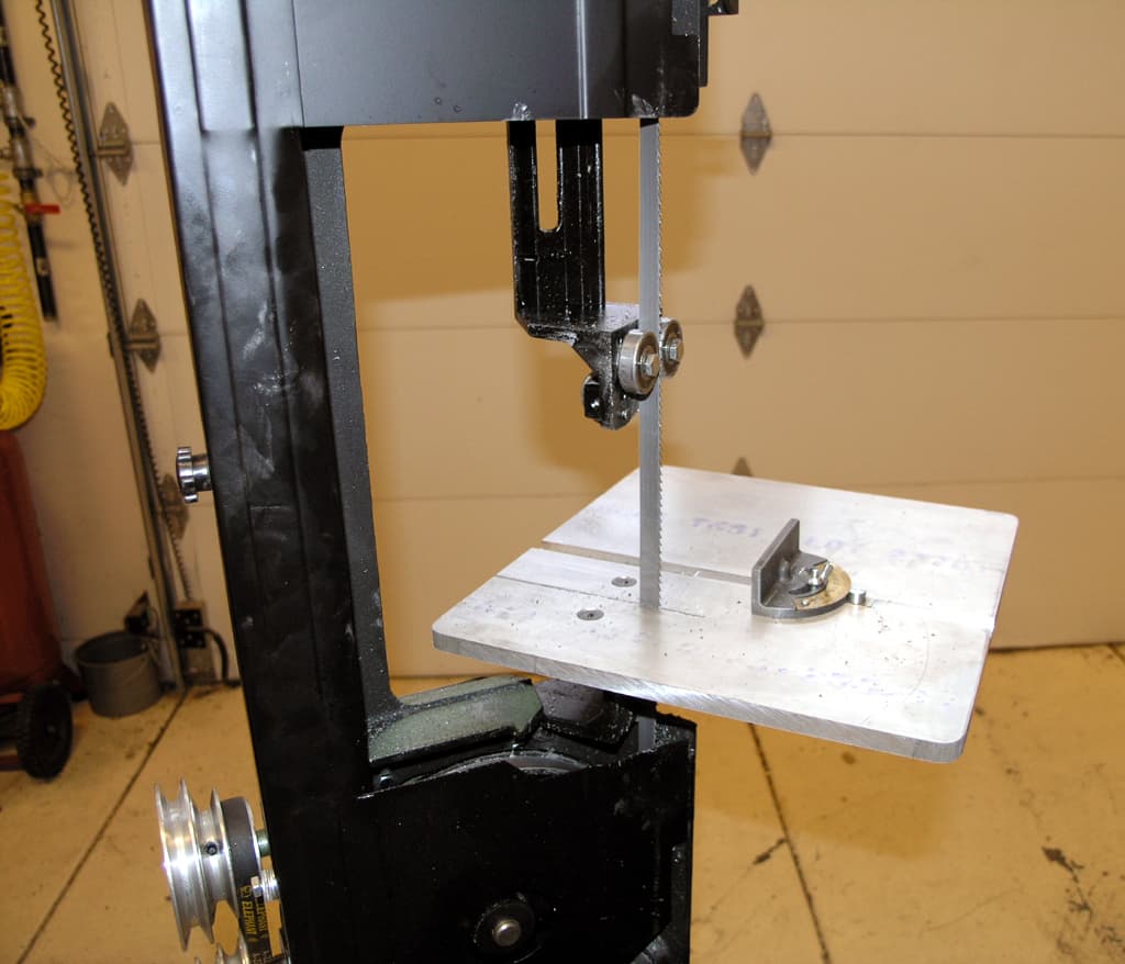 Mini vertical band saw in a workshop with a metal table and blade in focus.