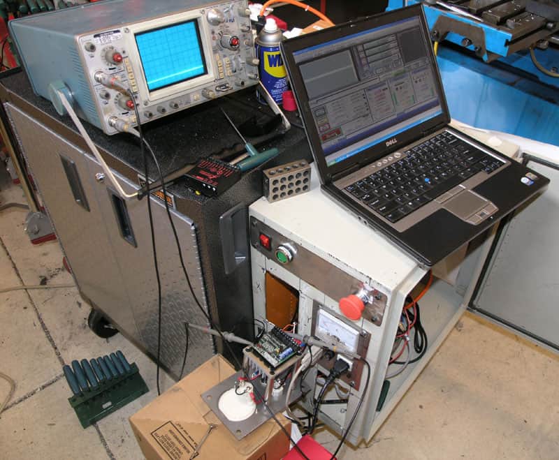 Cluttered workbench with various tools, oscilloscope, and machinery.