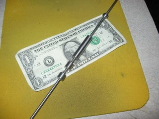 A photograph of a dollar bill being held by a metal rod.